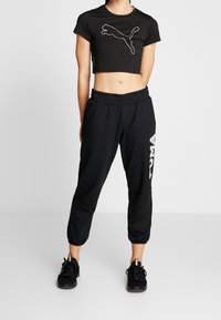 Zwarte crop top met wit Puma-logo, gecombineerd met zwarte joggerbroek met witte Puma-tekst. Beide kledingstukken hebben een losse pasvorm.