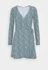 Långärmad omslagsklänning i mörkgrön med vitt blommönster, med v-ringning och knytning i midjan, tillverkad av mjukt material.