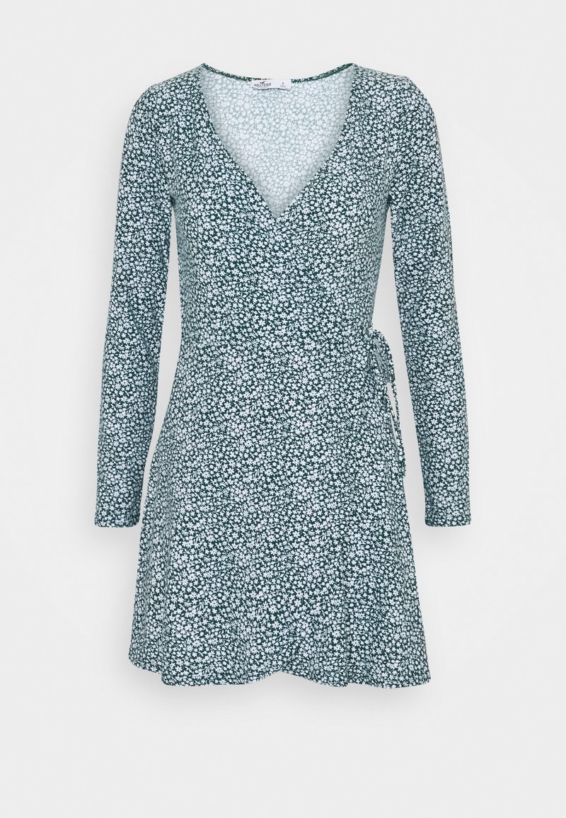 Dlouhý rukáv, zavinovací šaty v tmavě zelené barvě s bílým květinovým vzorem, s výstřihem do V a zavazováním v pase, vyrobené z měkké tkaniny.