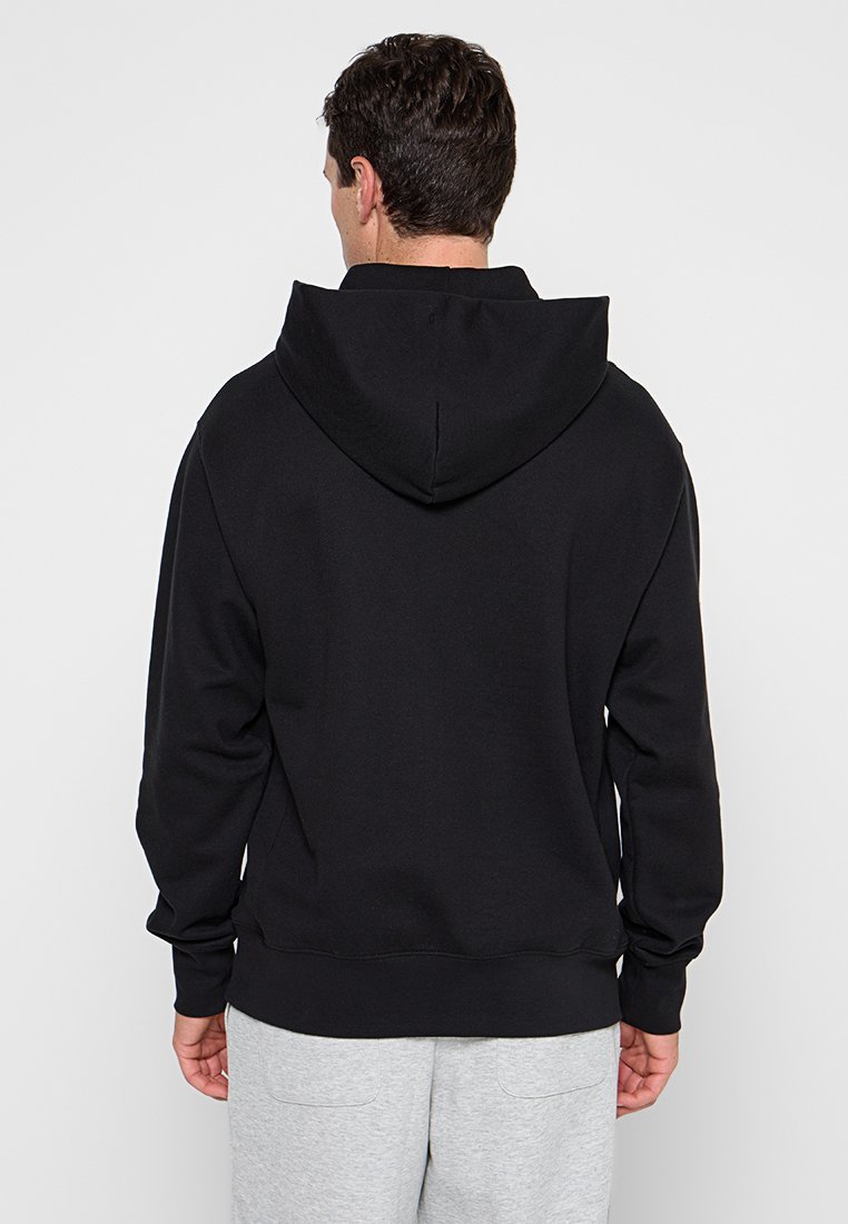 Schwarzer Kapuzenpullover mit Kängurutasche, gerippten Bündchen und Saum. Hergestellt aus weichem, strukturiertem Stoff und mit einem Etikett am hinteren Hals. 