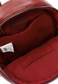 Intérieur d'un sac en cuir rouge avec doublure en tissu, poche intérieure plate, étiquette d'entretien et une étiquette de marque partiellement visible.