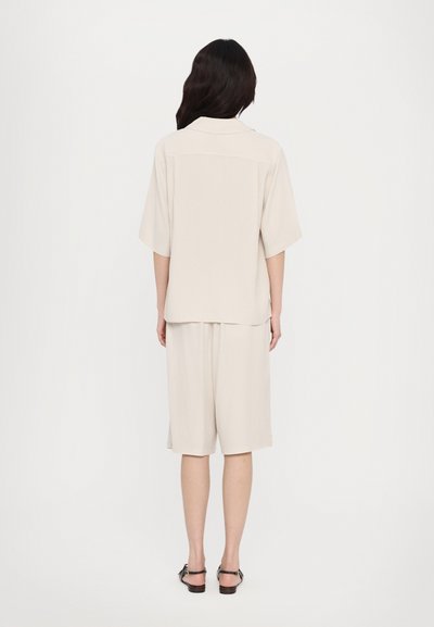 Beige kortærmet skjorte og matchende shorts i et glat, letvægtsstof. Enkel design med afslappet pasform og rygdetalje.
