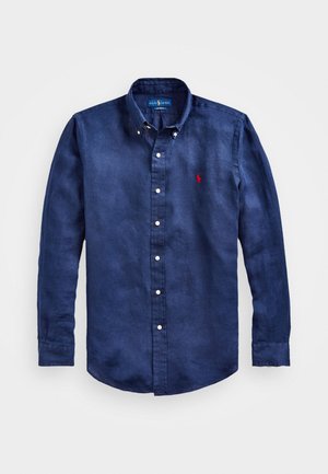 Chemise boutonnée à manches longues bleu marine en tissu doux, dotée d'un col classique et d'un petit logo rouge sur la poitrine gauche.