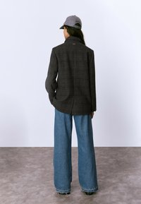 Blazer de cuadros gris con solapa, combinado con pantalones de mezclilla azul de pierna ancha con dobladillos deshilachados. Costuras visibles y ajuste relajado.