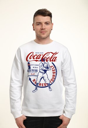 Sweatshirt blanc avec un graphisme vintage de Coca-Cola. Le design comprend un joueur de baseball rouge et bleu avec du texte et des accents.