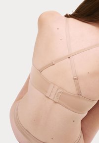 Beige trådlös bh med justerbara band och hake-och öga bakstängning. Slät tygstruktur med minimalistisk design.