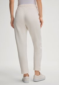 Light beige sweatpants featuring an elastic waistband, tapered legs, and side seam details. Paired with beige sneakers for a cohesive look.