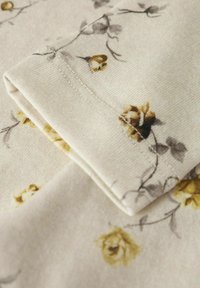 Salocīta auduma gabals ar beigu fona krāsu un dzeltenu un pelēku rožu ziedu rakstu. Tekstūra ir maiga, ar redzamām šuvju detaļām.