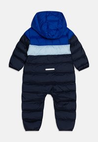 Tuta da neve imbottita blu e navy con cappuccio, caratterizzata da blocchi di colore orizzontali, una striscia riflettente e polsini a costine. Materiale resistente all'acqua.