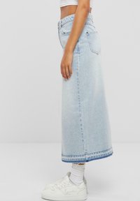 Vaaleansininen farkku maksihame, jossa on suora siluetti, kaksi takataskua ja huomaamaton repaleinen helma. Yhdistettynä valkoisiin lenkkareihin.