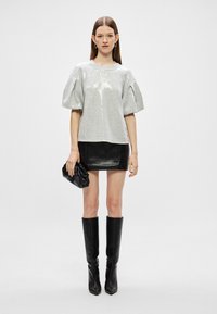 Hõbedane sequins'idega lühikeste varrukatega top puffvarrukatega, kombineeritud musta nahast mini seeliku ja põlve kõrguste mustade saapadega. Kotike käes.