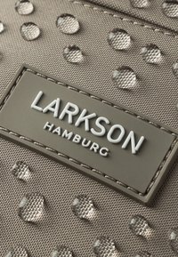 Tessuto grigio con una superficie texture caratterizzata da gocce rotonde e sollevate. Il nome del marchio "LARKSON" è stampato in bianco su un'etichetta grigia.