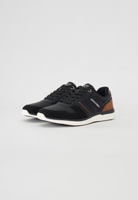 Black athletic shoes with leather and textile upper, white sole, brown accents, and lace-up design. Features logo on tongue.