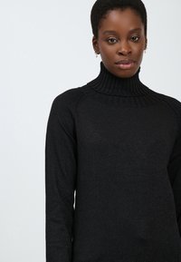 Schwarzer Rollkragenpullover mit geripptem Kragen, aus einem strukturierten Material gefertigt, mit langen Ärmeln und einer taillierten Passform.