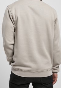 Light beige sweatshirt featuring a crew neck, ribbed cuffs and hem, and a soft texture, paired with black jeans.