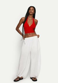 Rotes Halter-Crop-Top mit tiefem V-Ausschnitt und Raffung, kombiniert mit lockeren weißen weit geschnittenen Hosen und schwarzen Flip-Flops.