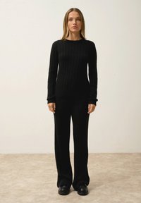 Ensemble de pull et pantalon en tricot côtelé noir. Manches longues, col rond, haut ajusté et pantalon décontracté à jambes larges. Texture lisse.