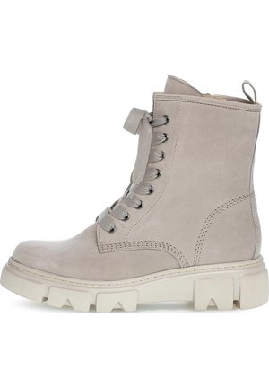 Jasnobeżowy zamszowy botek za kostkę na sznurowadła z grubą, masywną, kremowobiałą podeszwą oraz pętelką z tyłu.