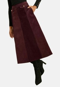 Gonna in corduroy bordeaux con una forma svasata, pieghe frontali e tasche laterali. Presenta due bottoni metallici sulla vita.