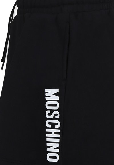 Pantaloni corti neri in morbido tessuto con cintura elastica e tasche laterali. Presentano un logo verticale bianco "MOSCHINO" sulla gamba sinistra.