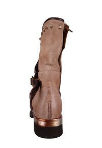 Zamszowy botek w kolorze beżowym z zaokrąglonym noskiem, brązowymi akcentami, metalowymi ćwiekami na górze oraz średniej wysokości drewnianym obcasem z metalicznym wykończeniem.