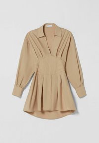 Beige blus med långa ärmar, djup V-ringning, rynkad midja och veckad byst. Mjuk kvalitet, knäppta ärmslut och rundad nederkant för en avslappnad passform.