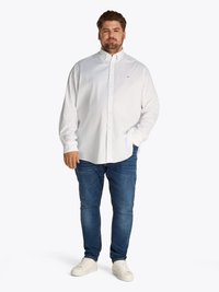Camisa blanca de algodón con botones, jeans azules y zapatillas blancas. Corte ajustado con cuello, que presenta un sutil branding en el pecho.