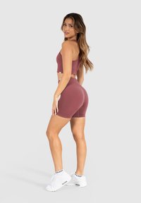 Bralette en high-waisted shorts in gedempt bordeaux, gemaakt van een gestructureerde stretchstof, gecombineerd met witte sportschoenen en enkelsokken.