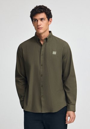 Olijfgroene overhemd met lange mouwen en een button-down kraag, textuurstof en een klein vierkant logopatch op de linkerkant van de borst.