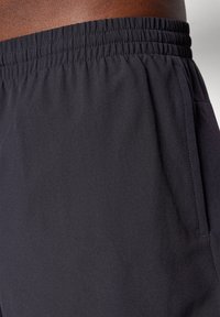 Sorte træningsshorts med elastisk talje, glat tekstur, sidelommer og et let, åndbart materiale.