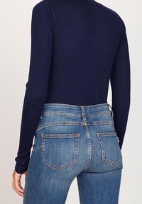 Marinblå långärmad topp med ribbat mönster, tillsammans med ljusblå högmidjade jeans med två bakfickor och synliga sömmar.