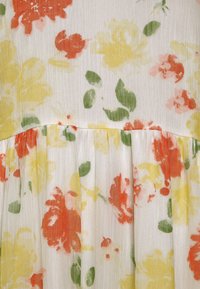 Tecido de vestido floral com um fundo branco e flores laranjas, amarelas e cor-de-rosa, complementadas por folhas verdes e detalhes plissados.