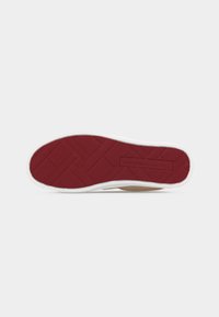 Suela de zapato con banda de rodadura de goma roja que presenta patrones geométricos y borde exterior blanco sobre un fondo claro y sencillo.