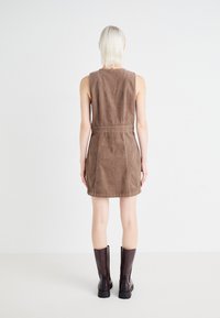 Vestito marrone senza maniche con vita aderente, realizzato in tessuto texturizzato, dotato di tasche posteriori e orlo dritto, abbinato a stivali al ginocchio.