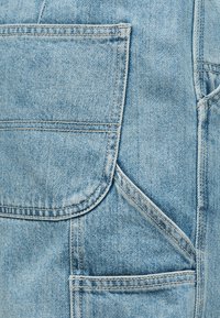 Υφασμα από ανοιχτό μπλε τζιν που δείχνει λεπτομερή ραφές και επικαλυπτόμενες τσέπες με ορατές ραφές.