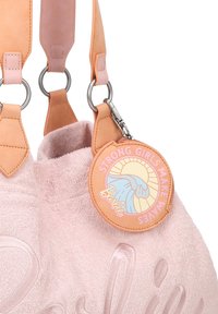 Roze badstof tas met leren handvatten, voorzien van een ronde label met de tekst "STERKE MEISJES MAKEN GOLVEN." Opmerkelijke details zijn de hardware ringen.