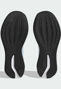 Semelles d'une paire de chaussures de course vues par en dessous avec une bande de roulement en caoutchouc noir et des accents blancs incurvés sur la semelle intermédiaire.