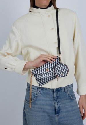 Clutch mit geometrischem Muster aus Stoff, versehen mit einer goldfarbenen Kette und einem runden Schlüsselanhänger. Farbschema: Grau, Schwarz und Weiß.