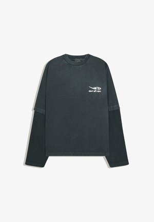 Chemise à manches longues grise foncée avec des manches courtes plus claires superposées sur des manches côtelées plus foncées, avec le texte "out of care" et un logo swoosh sur la poitrine.