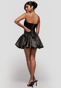 Zwarte strapless jurk met een nauwsluitend lijfje en een volumineuze satijnen rok. Heeft een striksluiting aan de achterkant en een gladde textuur. Hoge hakken maken de look compleet.