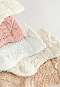 Calzini lavorati a maglia in colori pastello: rosa chiaro, crema, azzurro pallido e beige. Ognuno presenta un accento a fiocco e motivi testurizzati.