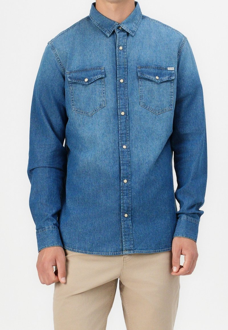 Camicia in denim blu con maniche lunghe, colletto a punta, due tasche sul petto e bottoni in metallo bianco. Texture liscia, design casual.
