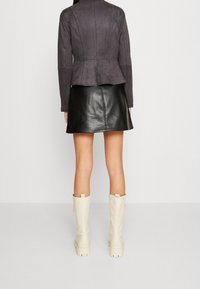 Giacca peplum in suede grigio con pannelli strutturati, abbinata a una minigonna in pelle nera e stivali bianchi al ginocchio. Materiali lisci e forme aderenti.