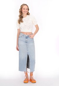Hvid cropped sweater med hjerte mønster, høj-taljede lyseblå denim nederdel med slids foran, og orange platform sandaler med ankelrem.