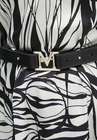 Cintura in pelle nera con una grande fibbia argentata a forma di "M", abbinata a un vestito con un audace motivo astratto di foglie in bianco e nero.
