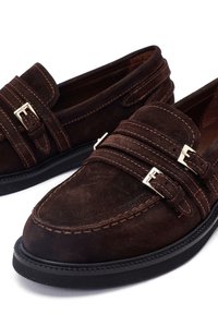 Mocassini in suede marrone con doppia fascia e dettaglio della fibbia, cuciture a contrasto e suola in gomma con finitura testurizzata.