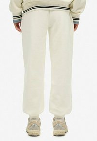Licht crème sweatpants met een relaxte pasvorm, voorzien van een elastische tailleband en boorden. Gecombineerd met beige sportschoenen.