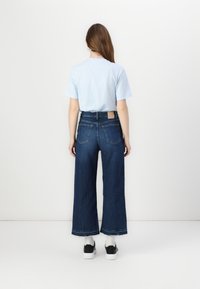 Un tricou din bumbac de culoare albastru deschis, asortat cu blugi din denim de culoare albastru închis, cu talie înaltă și croială largă. Prezintă un finisaj texturat și buzunare pe spate vizibile.