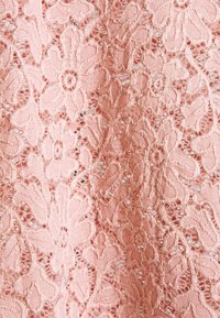 Tissu en dentelle florale rose avec des motifs de fleurs et de feuilles intriqués, présentant un délicat ouvrage ajouré et des broderies texturées.