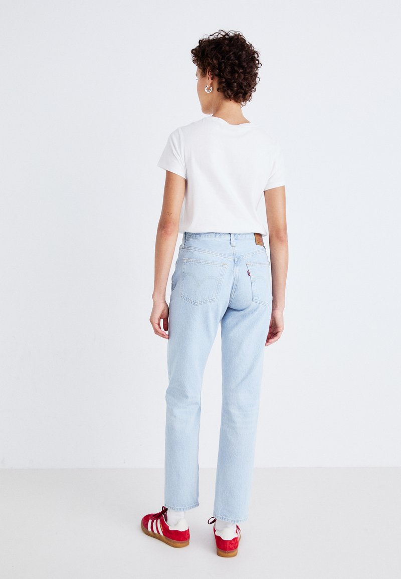 Jeans in denim azzurro chiaro con vestibilità dritta, caratterizzati da una toppa in pelle marrone sulla vita posteriore e cuciture minime sulle tasche posteriori.